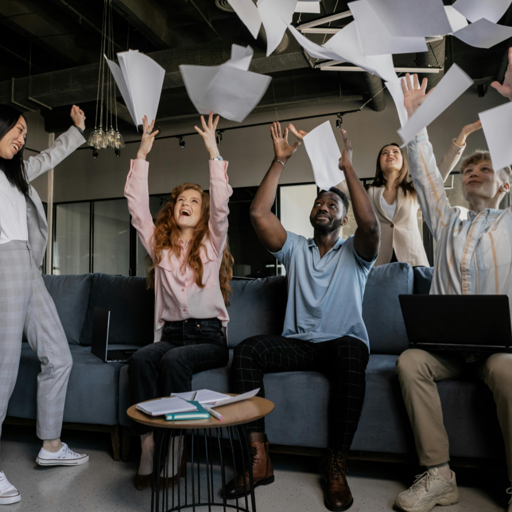 A group of people in a room celebrating improving their quality of work life by throwing papers in the air.