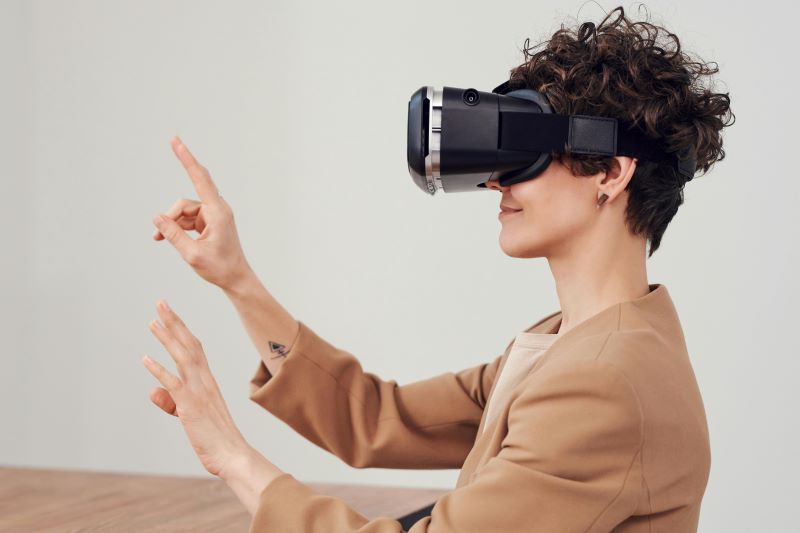 A person wearing a virtual reality headset extends their hands in front of them, interacting with something in virtual space. The individual has short, curly hair and is dressed in a beige jacket, possibly attending a professional training session in 2024.