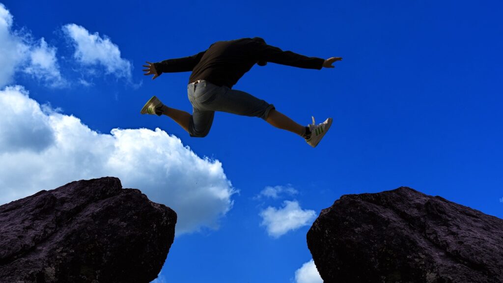 Une personne, mettant de côté toute peur, saute gracieusement entre deux gros rochers contre un ciel bleu parsemé de nuages.