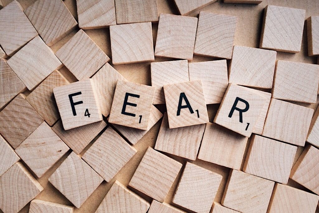 Wooden letter tiles arranged to spell "FEAR" against a scattered background of blank tiles form an intricate mosaic, subtly whispering "fear" in a universal language of emotion.