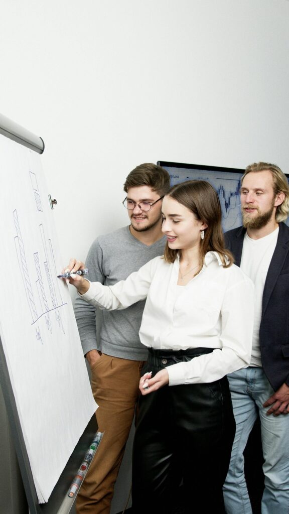 Trois personnes se tiennent debout à côté d'un tableau à feuilles mobiles dans un cadre professionnel. Une femme dessine un graphique linéaire illustrant les tendances liées à la santé mentale en entreprise tandis que deux hommes observent, plongés dans leurs pensées.