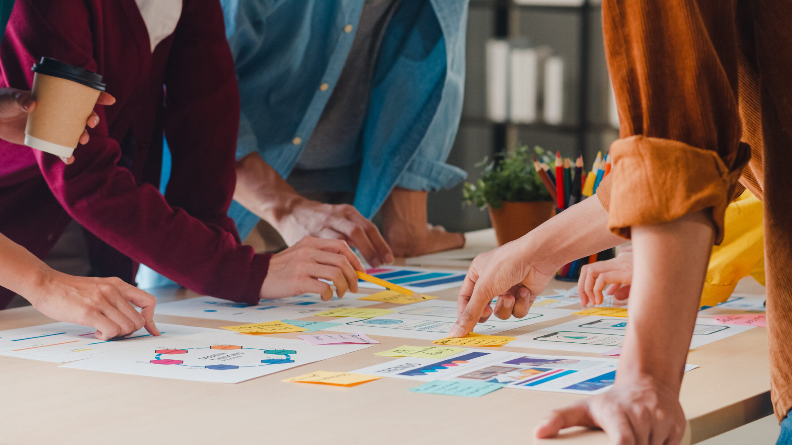 Un groupe de personnes collabore autour d’une table, pointant du doigt diverses notes et graphiques colorés essentiels à la mise en œuvre de Premiers Secours en Santé Mentale en entreprise. Une personne tient une tasse de café, alimentant leur concentration et leur créativité.